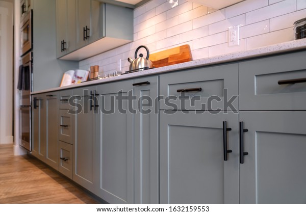 Kitchen cabinets with white countertop black\
handles and tile\
backsplash