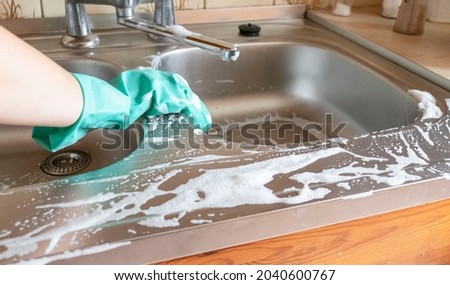 Kitchen cleaning. Woman in green protective rubber gloves cleaning kitchen furniture