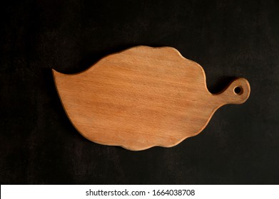 The kitchen composition. Beech cutting board in the shape of a leaf close-up on a dark concrete background.