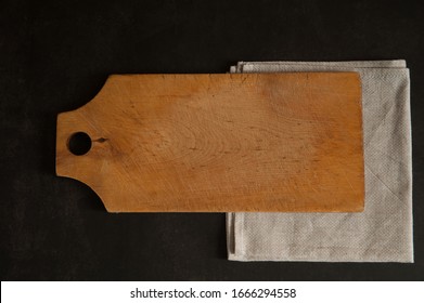 The kitchen composition. An old birch wood cutting board and a beige linen napkin close-up on a dark concrete background. 