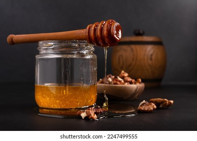 Kitchen composition of wooden barrel and glass jar with healthy organic honey, wooden dipper and bowl of walnuts on dark background - Powered by Shutterstock