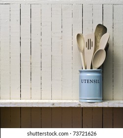 Kitchen Cooking Utensils; Wooden Spatulas Etc In China Storage Pot; On Wooden Shelf Against Rustic Kitchen Wall; Excellent Copy Space Over Wall Area