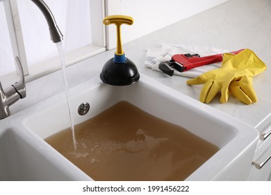 Kitchen counter with clogged sink, plunger and plumber's accessories