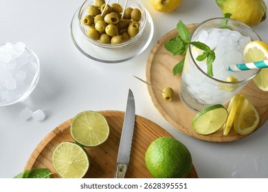 Kitchen counter with refreshing drink based on mint, lemon, and lime, with cutting board and fruit and containers with ice and olives. Top view.