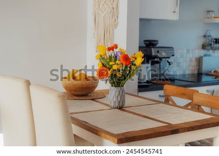 Kitchen counter table with focus on ceramic vase with multicolor various summer flower bouquet with blurred background of modern cozy white kitchen. Home interior design details