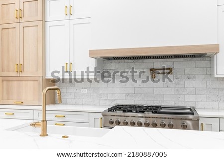 A kitchen detail shot with a gold faucet, white and wood cabinets, marble countertop, and subway tile backsplash.