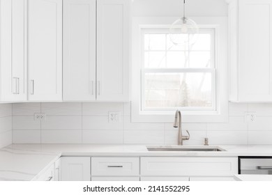 A Kitchen Detail Shot With White Cabinets, Wavy Subway Tile Backsplash, And A Glass Pendant Light Hanging Above The Sink And Window.