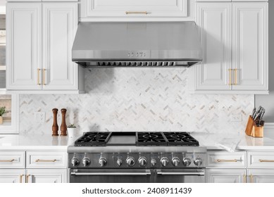 A kitchen detail of a stainless steel stove and range hood, granite countertops, and marble herringbone tile backsplash.