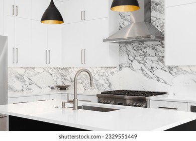 A kitchen detail with white cabinets, modern light fixtures hanging over a black island, and a marble countertop and backsplash.