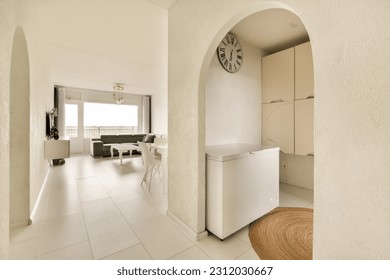 a kitchen and dining area in a house with white walls, floor tiles and an archway leading to the living room - Shutterstock ID 2312030667