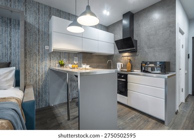A kitchen and dining area are shown in a small apartment. The space includes a countertop, stove, and dining items. Natural light enters through the windows