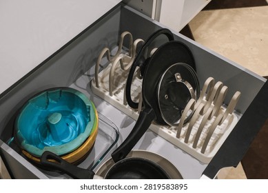 A kitchen drawer containing various cookware items. It includes a blue mixing bowl, several frying pans, and a pot organizer..
