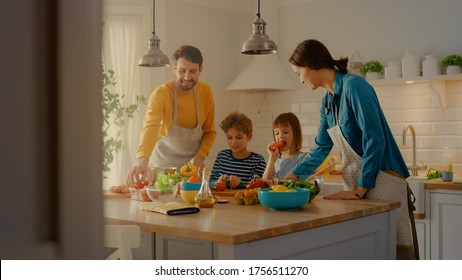 In Kitchen: Family Of Four Cooking Together Healthy Dinner. Mother, Father, Little Boy And Girl, Preparing Salads, Washing And Cutting Vegetables. Cute Children Helping Their Beautiful Caring Parents