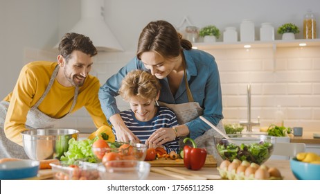 In Kitchen: Family Of Three Cooking Together Healthy Dinner. Mother And Fathe Teach Little Boy Healthy Habits And To Cut Vegetables For Dinner Salad. Cute Child Helping Their Beautiful Caring Parents