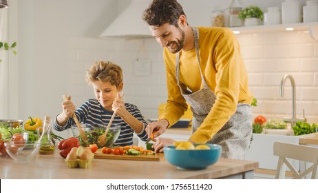 In Kitchen: Father And Cute Little Boy Cooking Together Healthy Dinner. Dad Teaches Little Son Healthy Habits And How To Mix Vegetables In Salad Bowl. Cute Child Helping His Beautiful Caring Parents