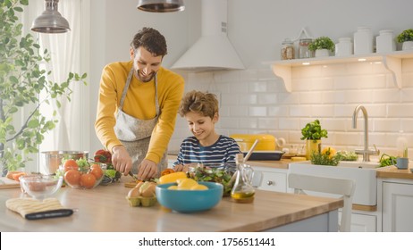 In The Kitchen: Father And Cute Little Son Cooking Together Healthy Dinner. Dad Teaches Little Boy Healthy Habits And How To Cut Vegetables For The Salad. Happy Child And Parent Spend Time Together