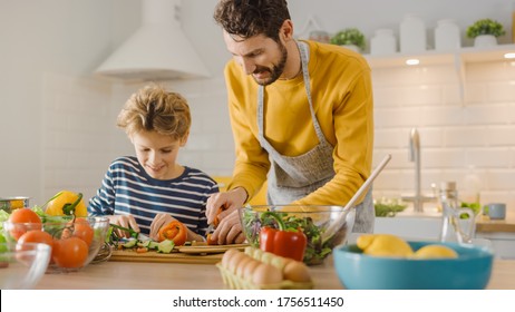 In The Kitchen: Father And Cute Little Son Cooking Together Healthy Dinner. Dad Teaches Little Boy Healthy Habits And How To Cut Vegetables For The Salad. Happy Child And Parent Spend Time Together