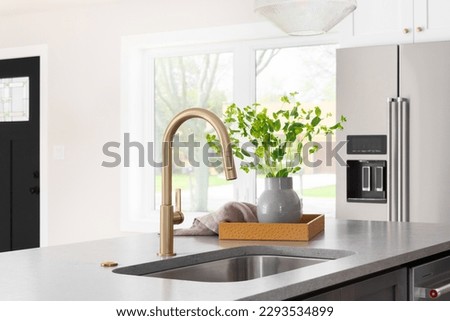A kitchen faucet detail with a grey stone countertop island, gold faucet, stainless steel appliances, and white cabinets.