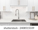 A kitchen faucet detail with white cabinets, gold hardware, and a subway tile backsplash.