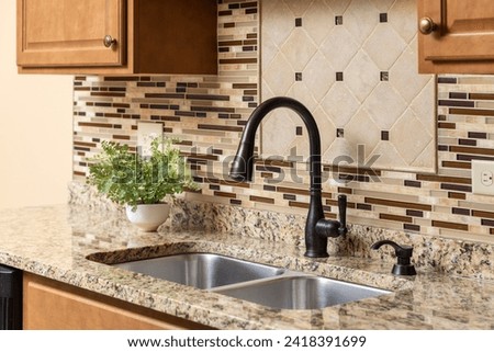 A kitchen faucet detail with wood cabinets, an oil rubbed bronze faucet, quartz countertop, and glass and stone tile backsplash.