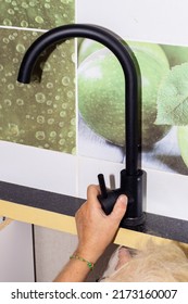 Kitchen Faucet Installation. A Man Is Screwing A Black Faucet To The Kitchen Countertop. Repair In The House.