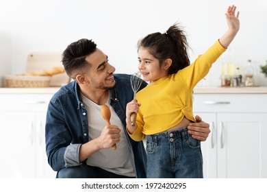 Kitchen Fun. Cheerful Young Arab Dad And His Little Daughter Singing While Cooking Food Together At Home, Using Whisk And Spatula As Microphone, Cute Preschooler Girl Fooling With Father, Closeup