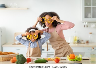 Kitchen Fun. Portrait Of Funny Black Woman And Little Girl Playing With Food, Making Glasses Of Sweet Pepper Fooling Around Together, Cooking Fresh Healthy Meal For Family, Preparing Vegan Salad