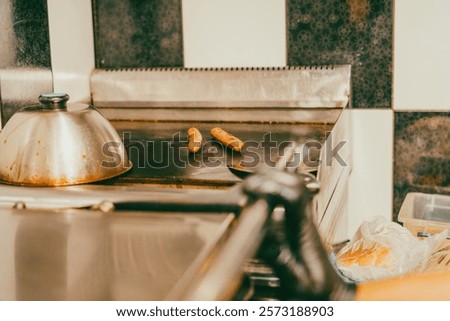 A kitchen with a grill and a pot on it. A pair of hot dogs are on the grill