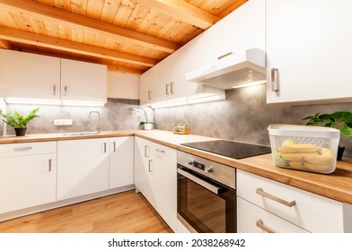 Kitchen at home with concrete texture on wall, white cabinets, regular appliances and wooden work top, floor and ceiling. Kitchen is decorated with flowers and illuminated with led lights. - Shutterstock ID 2038268942