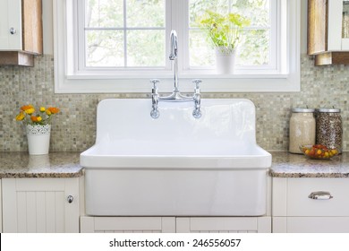 Kücheninnenraum mit großem rustikalem weißem Porzellansinfektionsbecken und Granitsteindecke unter sonnigem Fenster