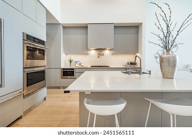 Kitchen interior of a waterfront condo light grey cabinets white granite countertop stove and range hood sink hardwood floor view to ocean through floor to ceiling windows butler pantry wine fridge - Powered by Shutterstock