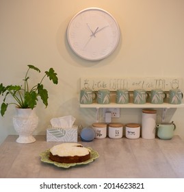 Kitchen Island Bench With Coffee Cups, Clock, Alexa Speaker, House Plant And Iced Cake 