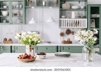 Kitchen Island With Marble Surface, Small Bowl Of Cherries With Bigger Wooden Bowl Filled With Strawberry, Flowers In Bucket And Glass Jar, Green Vintage Cupboards Full Of Different Devices