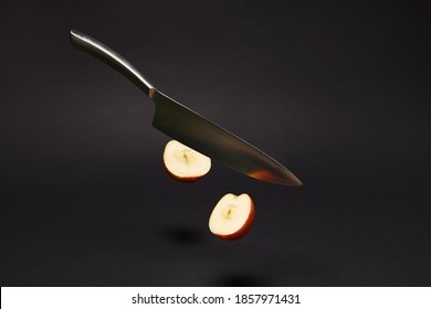 A  Kitchen Knife In Gravity Cuts An Apple In Half Isolated On Black Background.