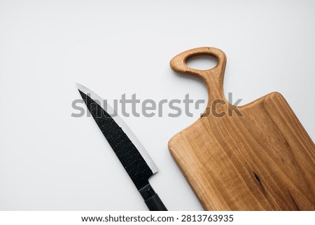 Kitchen knife placed next to a handmade walnut cutting board isolated on white background. Minimal studio product composition with wooden kitchenware and steel blade for cooking.