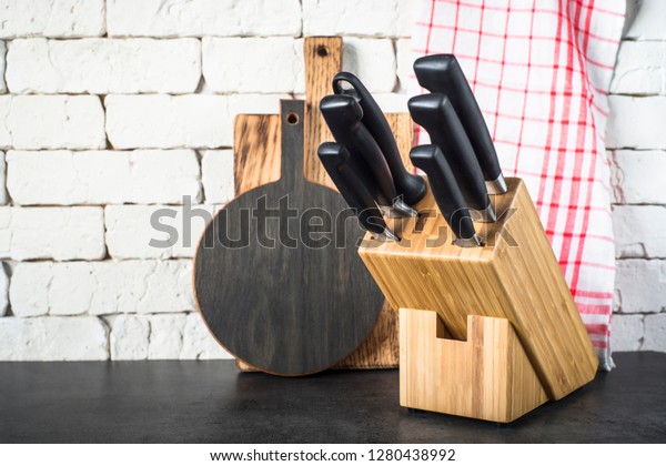 Kitchen\
knives set in the wooden block, cutting boards and towel on the\
kitchen  black stone table near the brick\
wall.