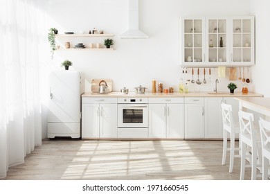 Kitchen with light walls, white furniture and shelves with crockery and plants in pots, small refrigerator in dining room scandinavian design, empty space. Modern interior with sunbeams on the floor