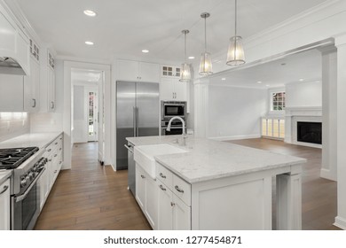 Kitchen And Living Room In New Luxury Home With Hardwood Floors, Farmhouse Sink, Stainless Steel Refrigerator, And Built-Ins With Backlight.