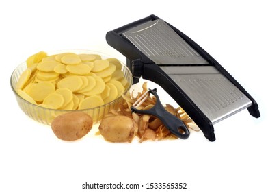 Kitchen mandolin next to a vegetable peeler and a bowl of sliced raw potatoes