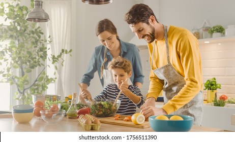 In The Kitchen: Mother, Father And Cute Little Boy Cooking Together Healthy Dinner. Parents Teach Little Son Healthy Habits And How To Mix Vegetables In The Salad Bowl. Cute Child Helping His Parents