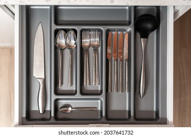 Kitchen with nobody, clean tableware in drawer. Cutlery set for home, open domestic storage with kitchenware. Closeup flatlay with metal domestic furniture, spoon, fork and knife.