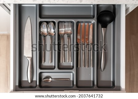 Kitchen with nobody, clean tableware in drawer. Cutlery set for home, open domestic storage with kitchenware. Closeup flatlay with metal domestic furniture, spoon, fork and knife.