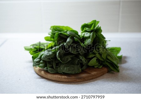 In the kitchen, on the table, there are bunches of green, fresh spinach and sorrel leaves on a wooden cutting board.