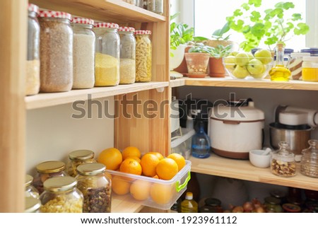 Kitchen pantry, wooden shelves with jars and containers with food, food storage. Jars of cereals, container of oranges, kitchen utensils, houseplants
