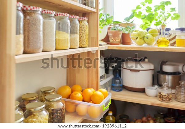 Kitchen pantry, wooden shelves with jars and
containers with food, food storage. Jars of cereals, container of
oranges, kitchen utensils,
houseplants