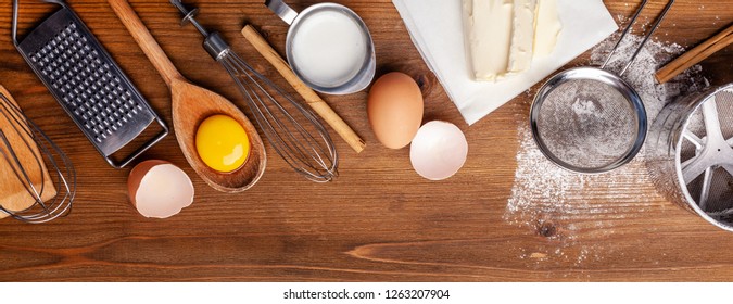 Kitchen, pastry inventory lies on the wooden table. Butter, eggs, wooden spoons, whisk, flour, milk. Top view with copy space, mockup for menu, recipe for culinary classes. Banner - Powered by Shutterstock