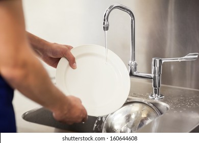 Kitchen porter cleaning white plates in sink in professional kitchen - Powered by Shutterstock