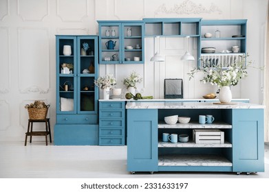 Kitchen in scandinavian style with island table, blue furniture and modern kitchenware. Bright interior with white walls and floor. Vase with flowers on marble countertop.