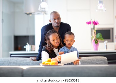 Kitchen Setting With Young Black Family Playing With A Tablet Pc.