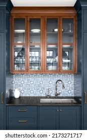 A Kitchen Sink With A Beautiful Pattern Tiled Backsplash With A Chrome Faucet, Black Granite Countertops, And Surrounded By Blue And Wood Cabinets.